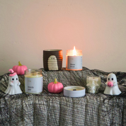 A styled collection of Halloween-themed candles and decorative items arranged on a black spiderweb-covered table against a beige wall. 