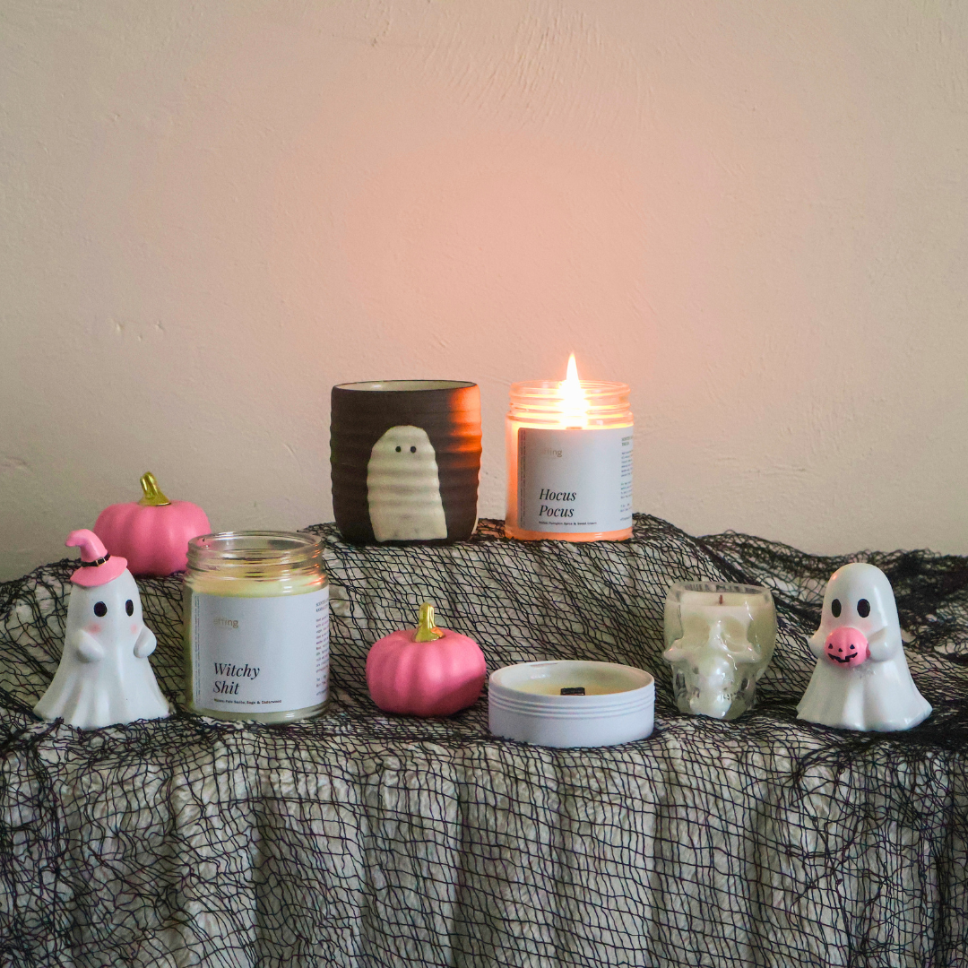 A styled collection of Halloween-themed candles and decorative items arranged on a black spiderweb-covered table against a beige wall.