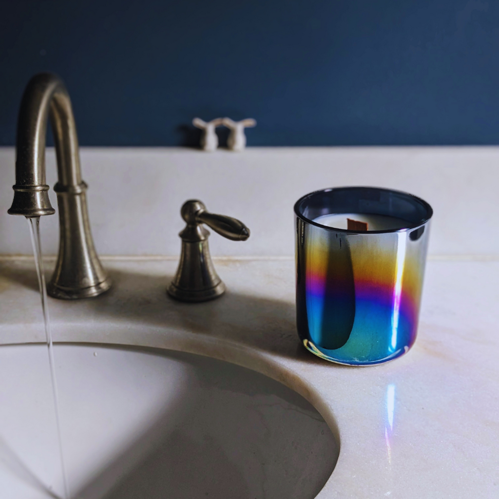 effing candle co iridescent black candle on a white quartz bathroom vanity ledge next to a brushed silver faucet that is running