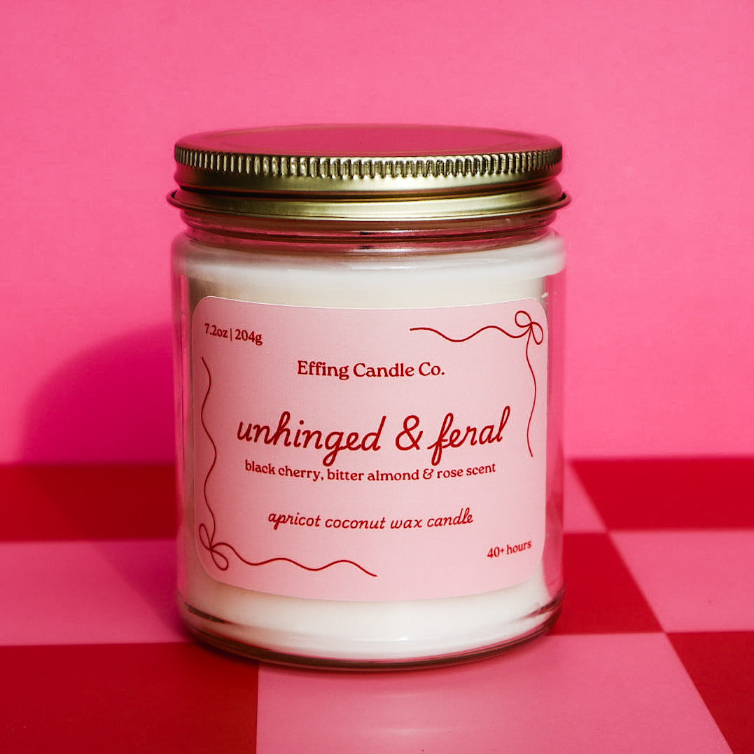 Candle jar that says Unhinged and Feral with a pink label on a red and pink checkered background